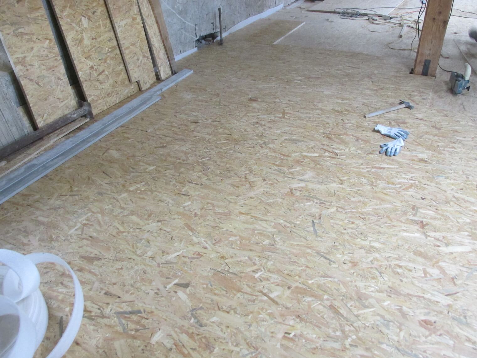 Una stanza con un pavimento in legno e una scala sullo sfondo.