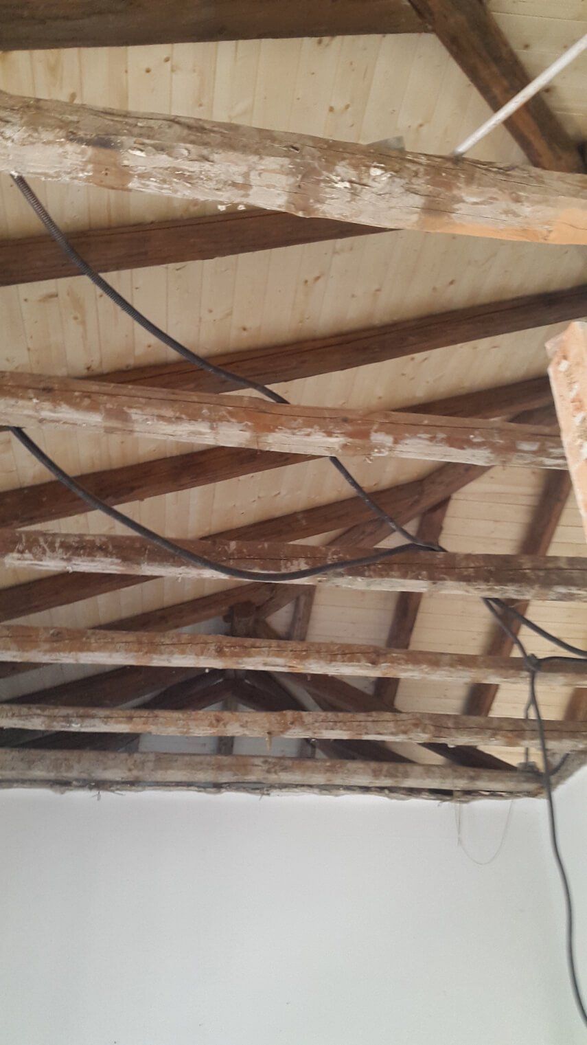 Un soffitto con travi di legno e fili che pendono da esse.