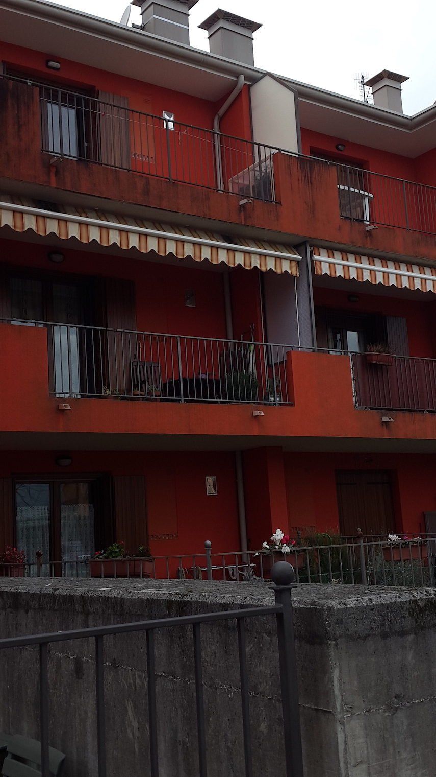 Un edificio rosso con balconi e una recinzione di fronte