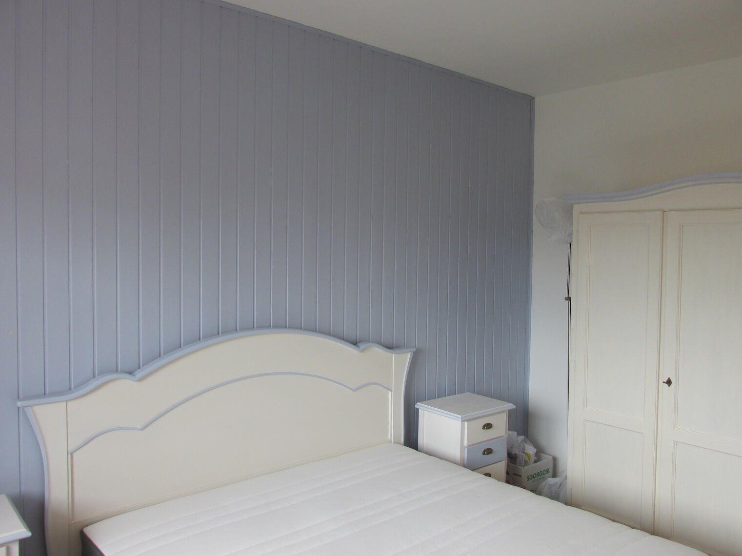 Una camera da letto con un letto bianco e una parete grigia