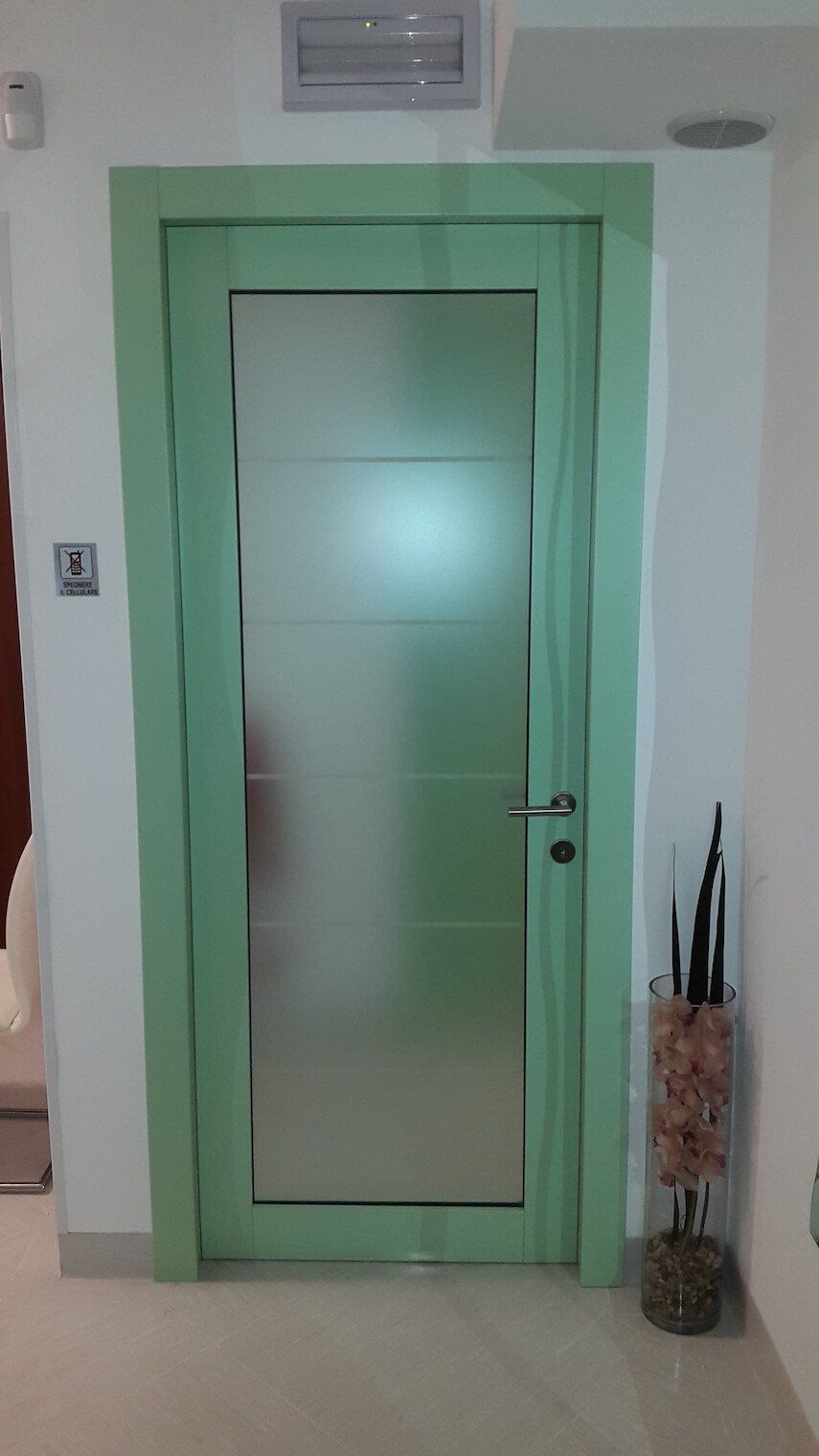 Una porta verde con un pannello di vetro smerigliato si trova nel corridoio, accanto a un vaso di fiori.