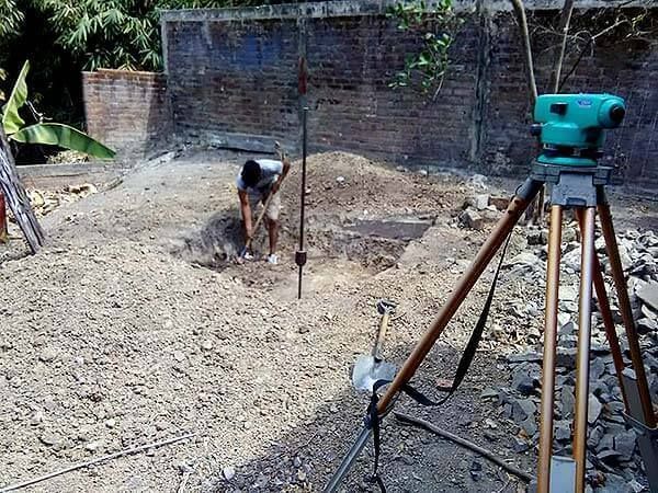 Un hombre está cavando en la tierra al lado de un trípode.