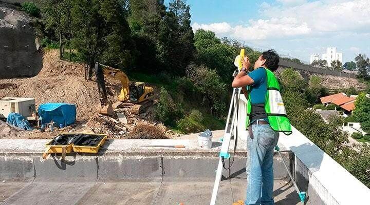 Un hombre con un chaleco verde está de pie en un tejado mirando a través de un telescopio.