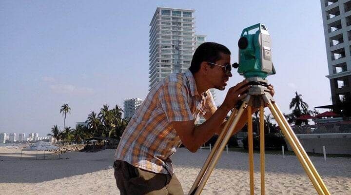 Un hombre está mirando a través de un telescopio en un trípode en la playa.