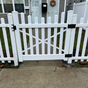 A white vinyl picket fence with a centered swinging gate in front of a residential home entrance.