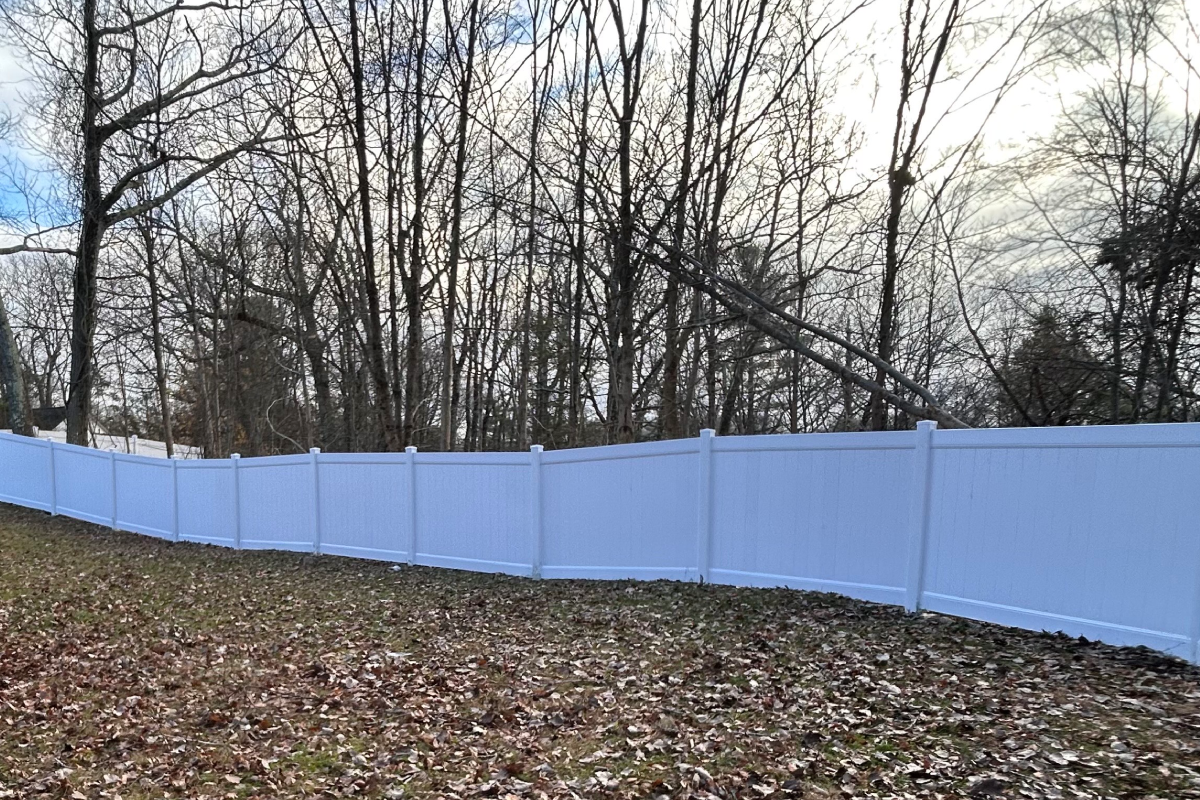 Woman in straw hat smiles, holding wine glass near a lake.