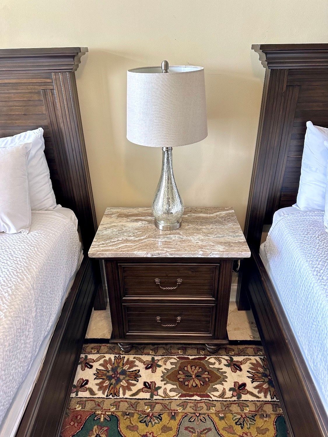 A bedroom with two beds and a nightstand with a lamp on it.