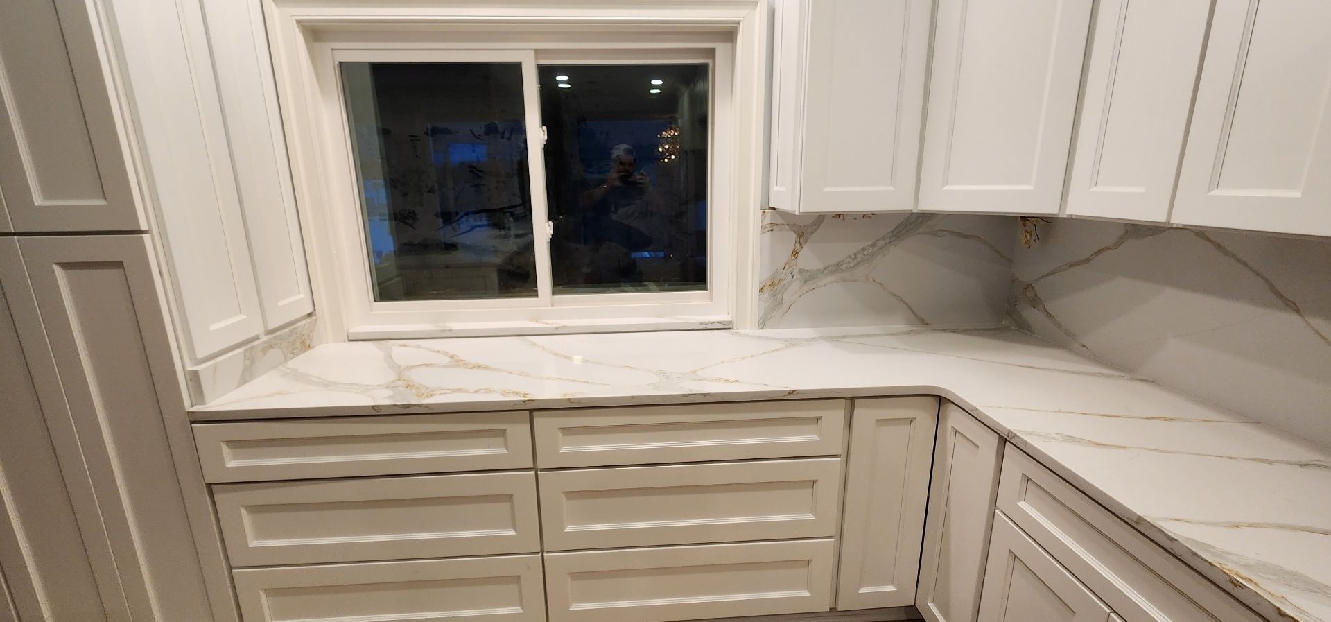 A kitchen with white cabinets and marble counter tops and a window.