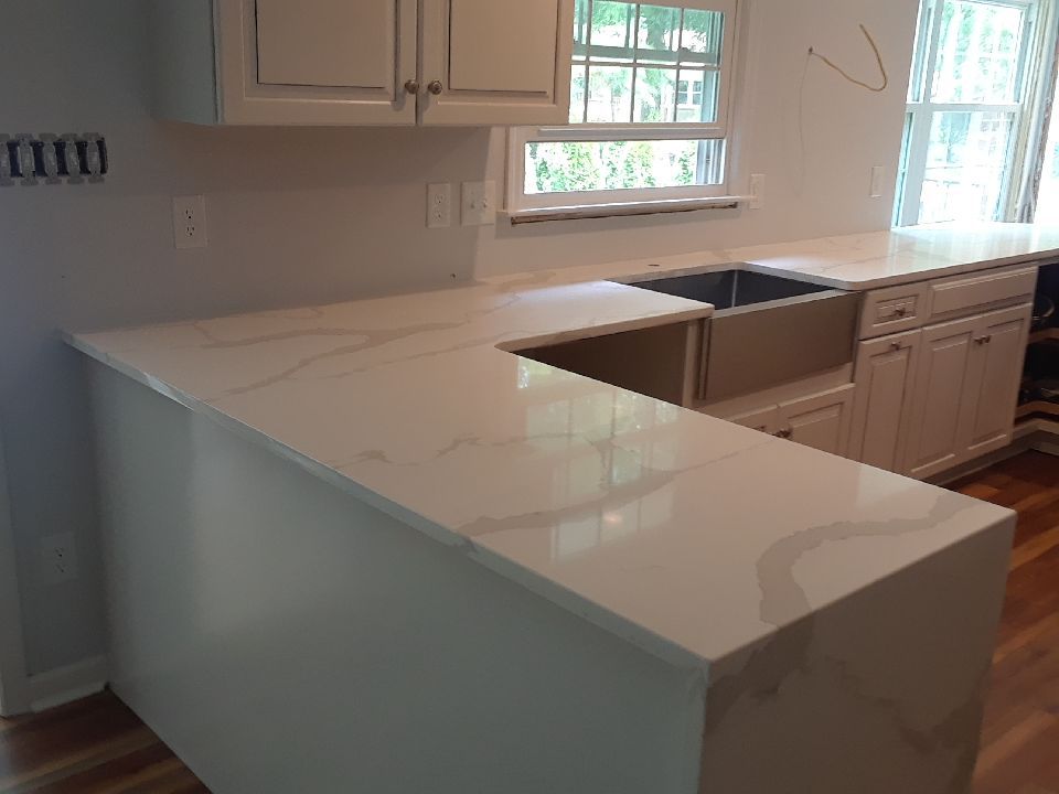 A kitchen with white cabinets , white counter tops , a sink and a window.