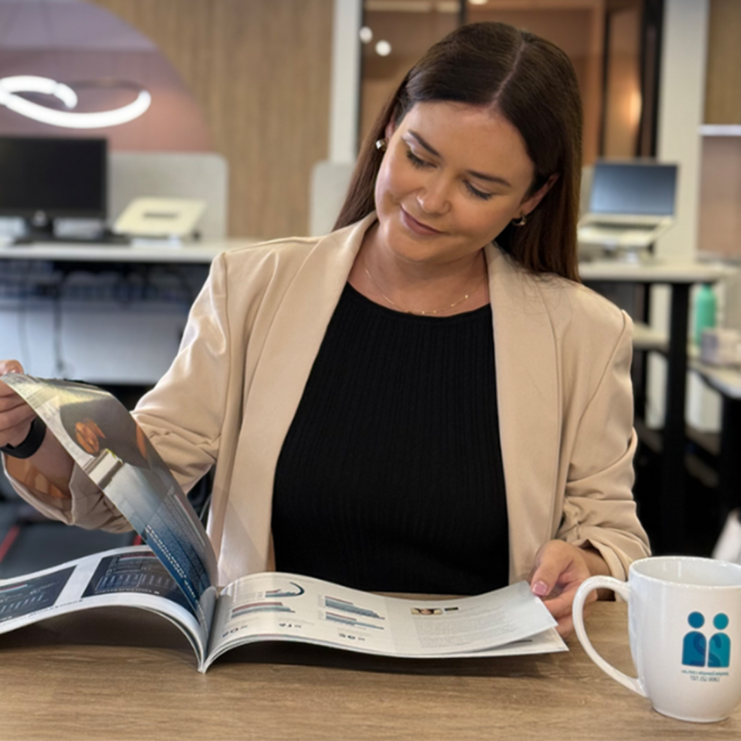 Woman in blazer looking at a catalog, seated at a desk with a mug.