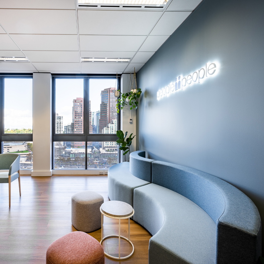 Modern office waiting area with curved sofa, small stools, and city views. Neon sign reads 