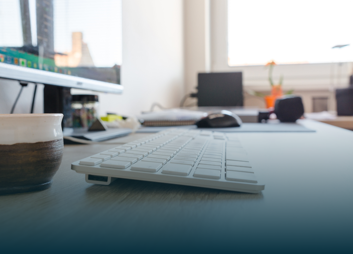 White keyboard on a desk; a mug, computer, and laptop are also visible.