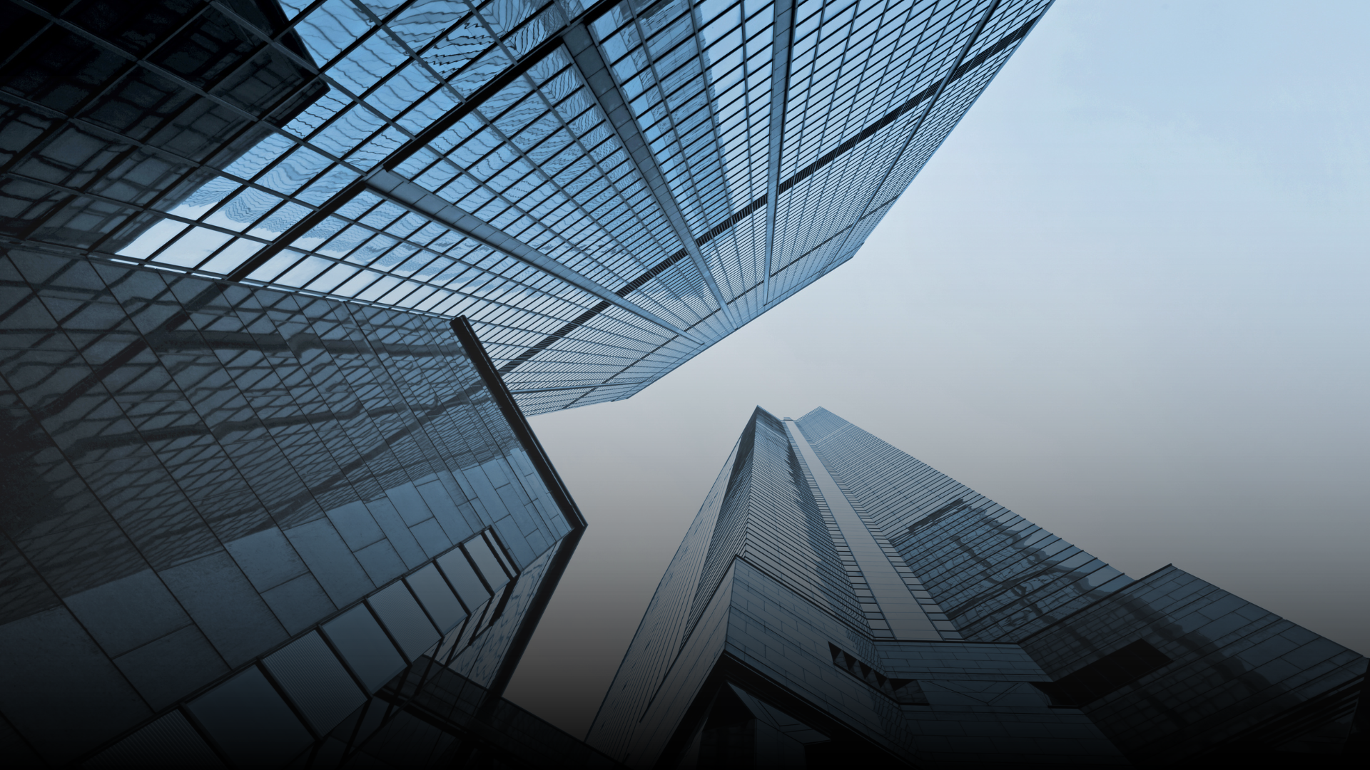 Low-angle view of tall, modern skyscrapers with glass facades against a light blue sky.