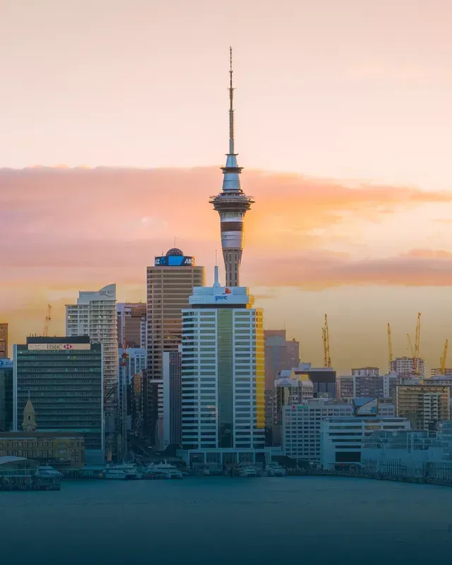 Auckland, New Zealand skyline with the Sky Tower at the center under a pastel sunset.