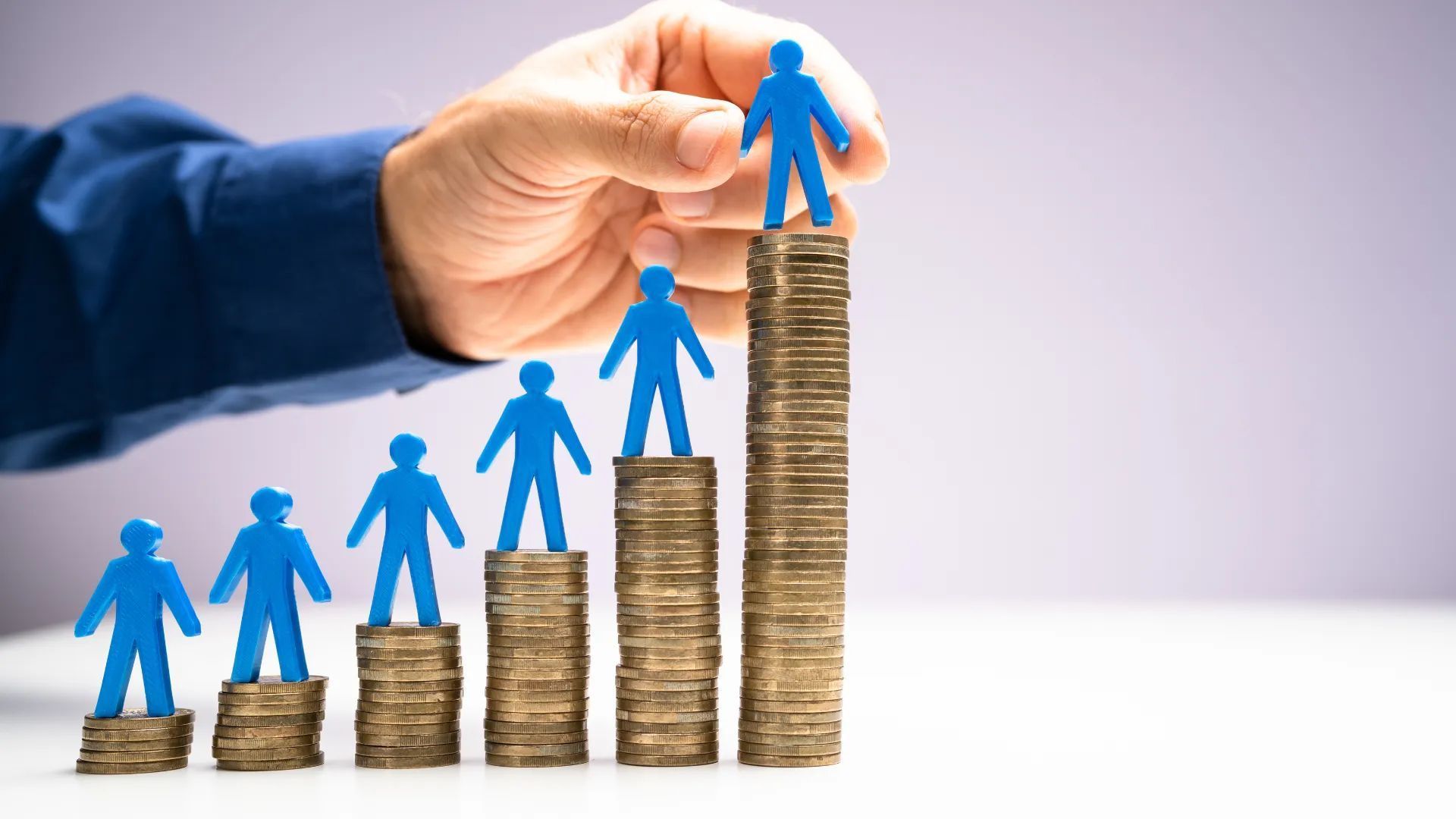 Hand placing blue figure on top of coin stacks, representing career advancement.