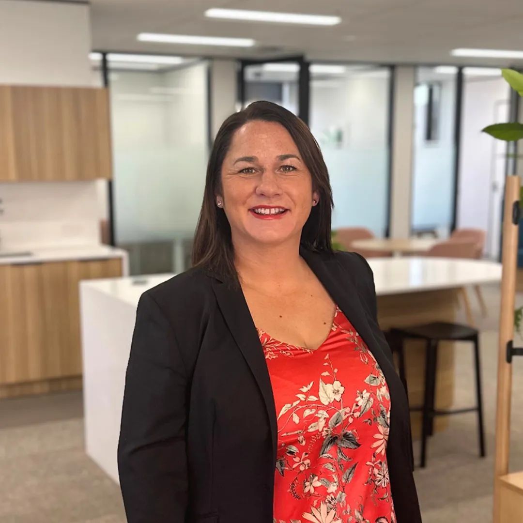 Woman in blazer and red patterned top smiles in an office setting.