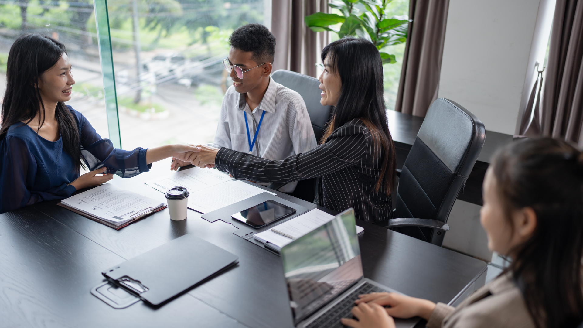 People shaking hands at a conference table with documents and laptops.