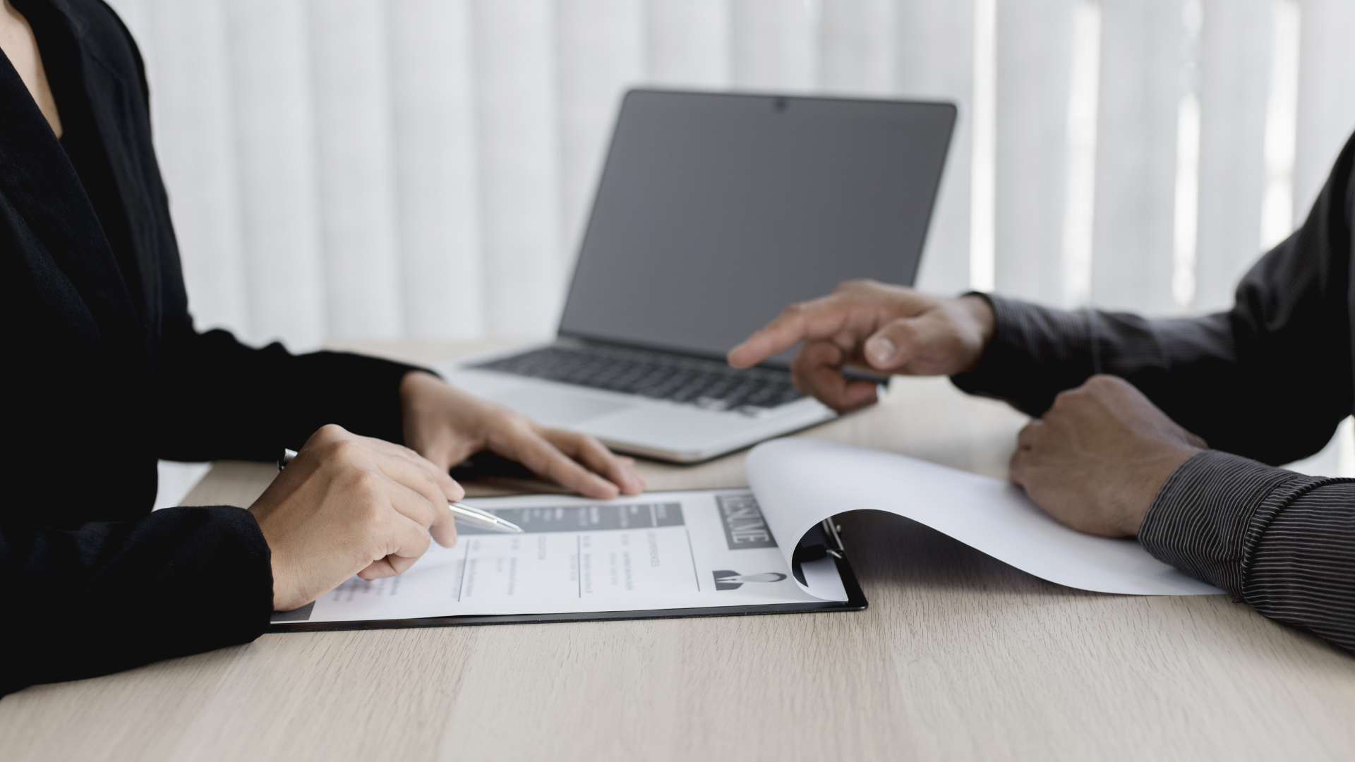 Two people at a desk review documents; one points, a laptop sits between them.