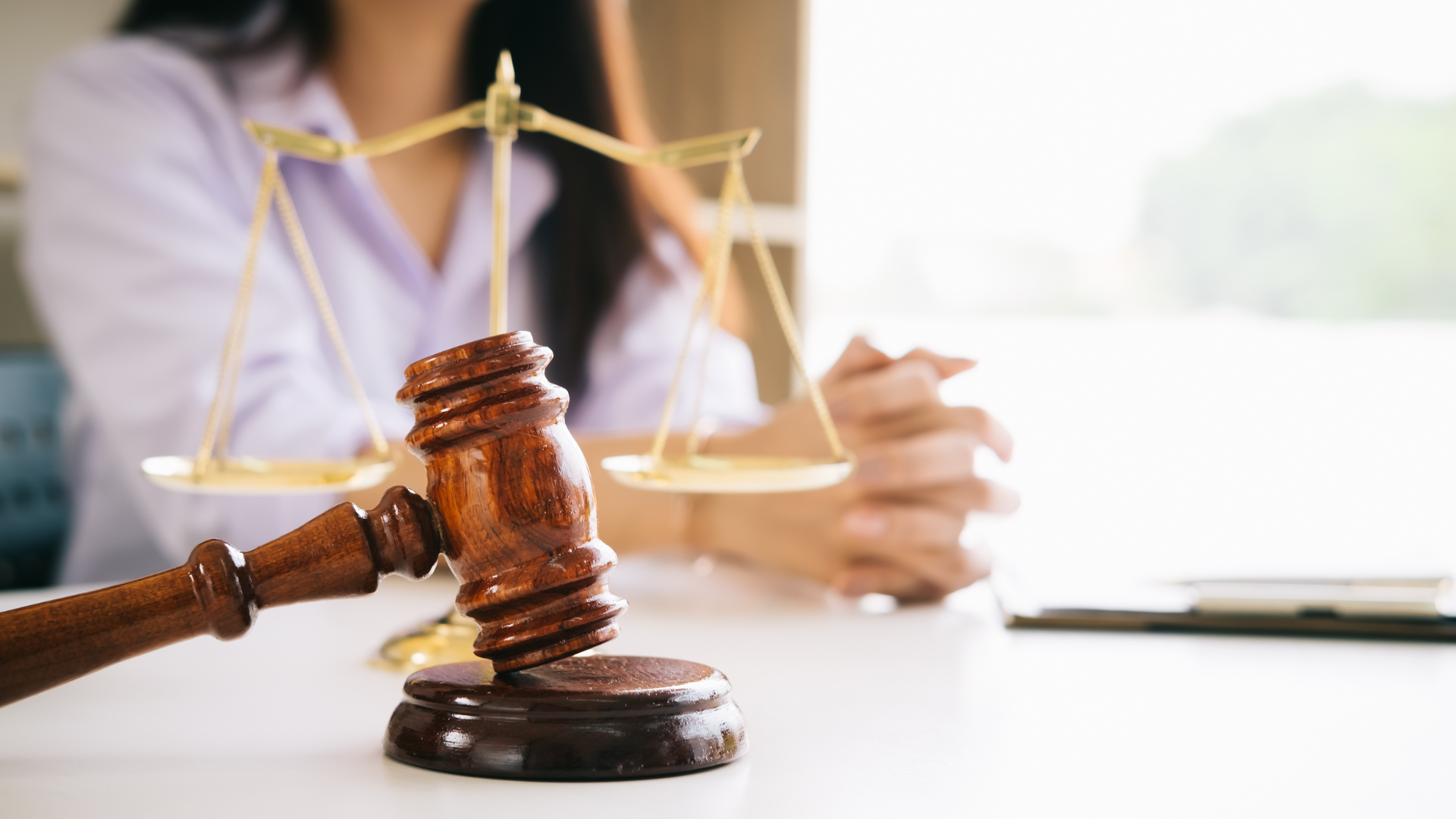 Wooden gavel on a table with a person and scales of justice in the background.
