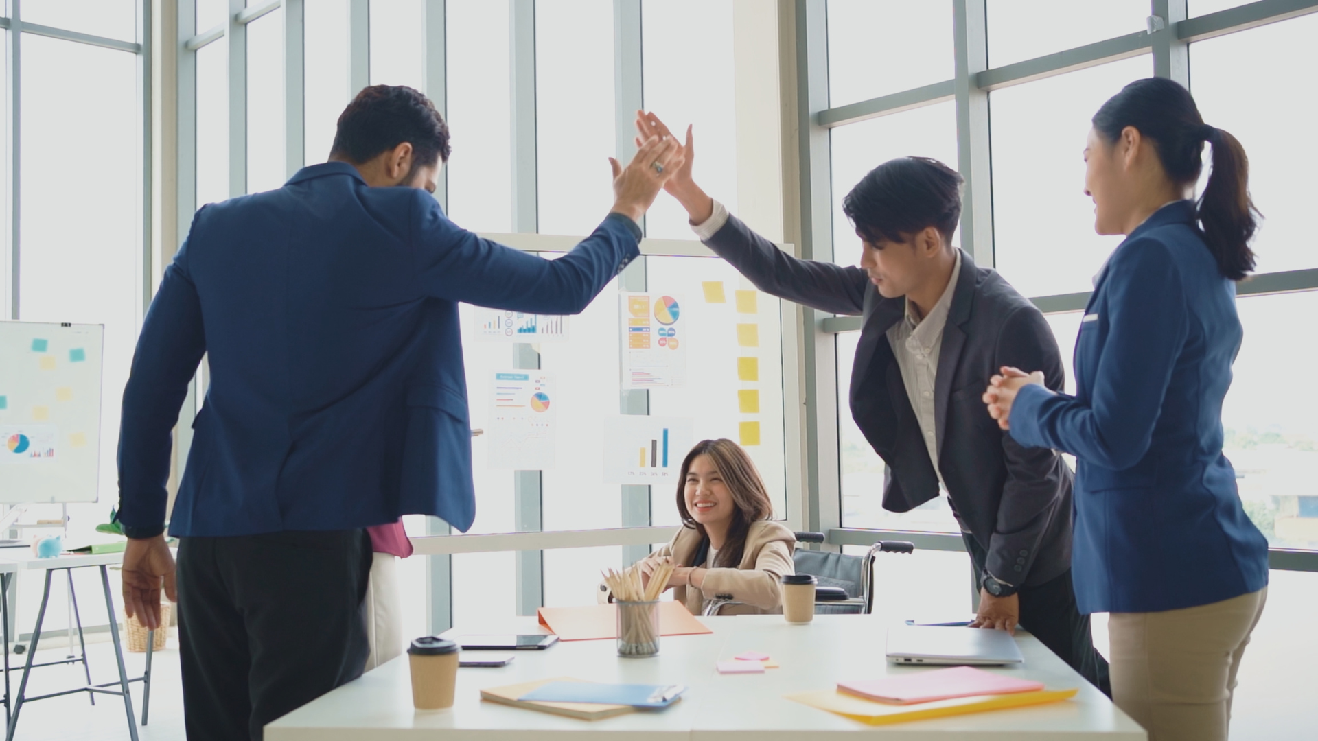 Business colleagues high-fiving in a light-filled office, celebrating a success.