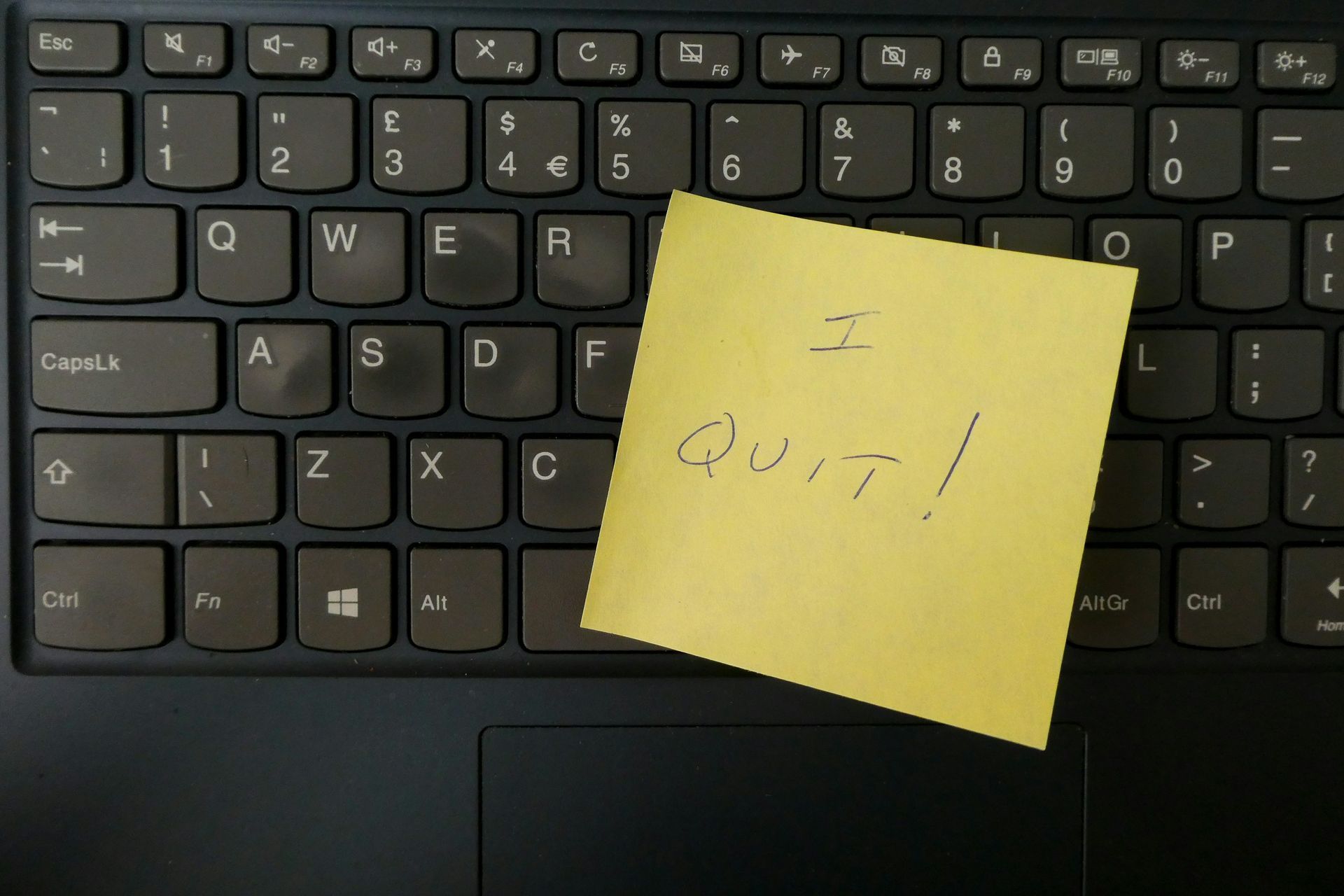 Yellow sticky note on a black laptop keyboard; text reads, 