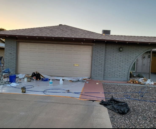 House with garage and brick wall undergoing exterior painting. Equipment, tarps, and supplies are on the ground.