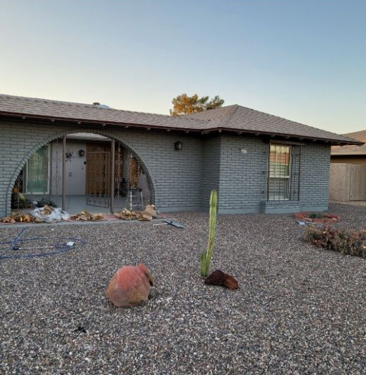 A one-story brick house with gravel yard, a potted cactus and a large arched entry.