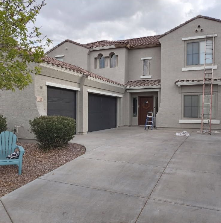 Two-story stucco house with gray garage doors, a ladder, and a driveway.