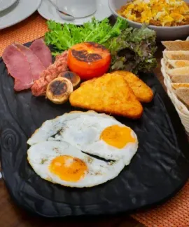 Breakfast plate with fried eggs, toast, bacon, hash browns, grilled tomato, mushrooms, and jam packets