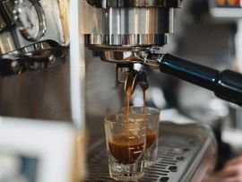 Espresso machine pouring coffee into a small glass cup on a metal drip tray.