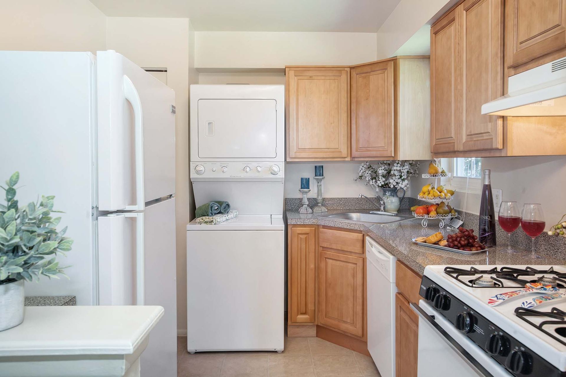 Compact kitchen with stacked washer/dryer, wooden cabinets, sink, and stove.