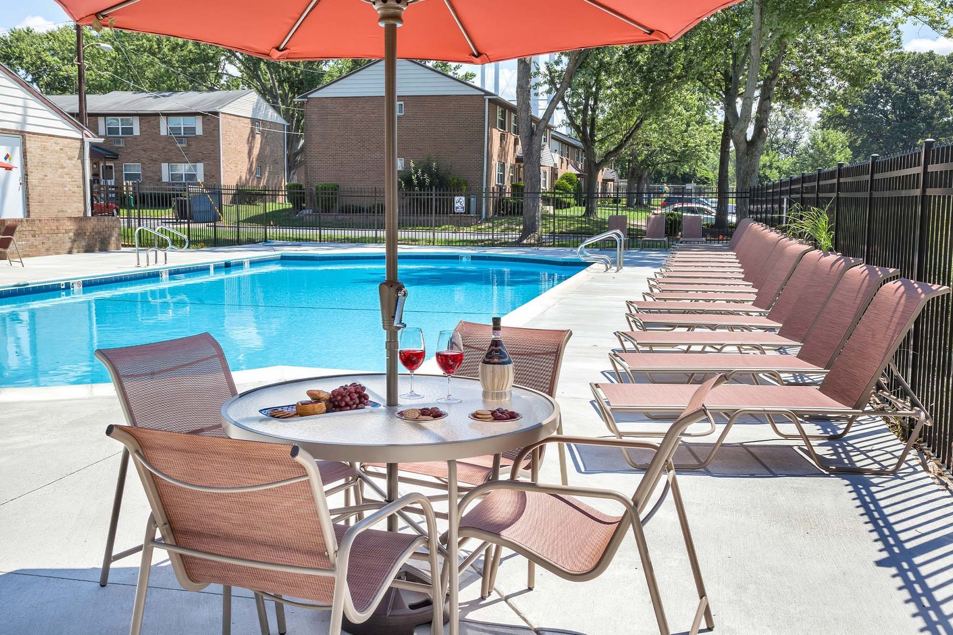 Outdoor pool area with lounge chairs and an umbrella at a multifamily community.