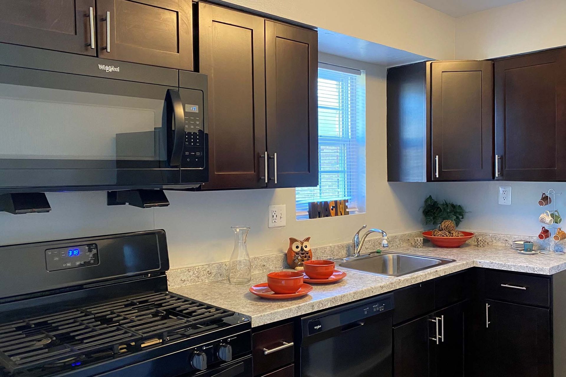 Kitchen with dark wood cabinets, granite counters, and stainless appliances surrounding a sink.