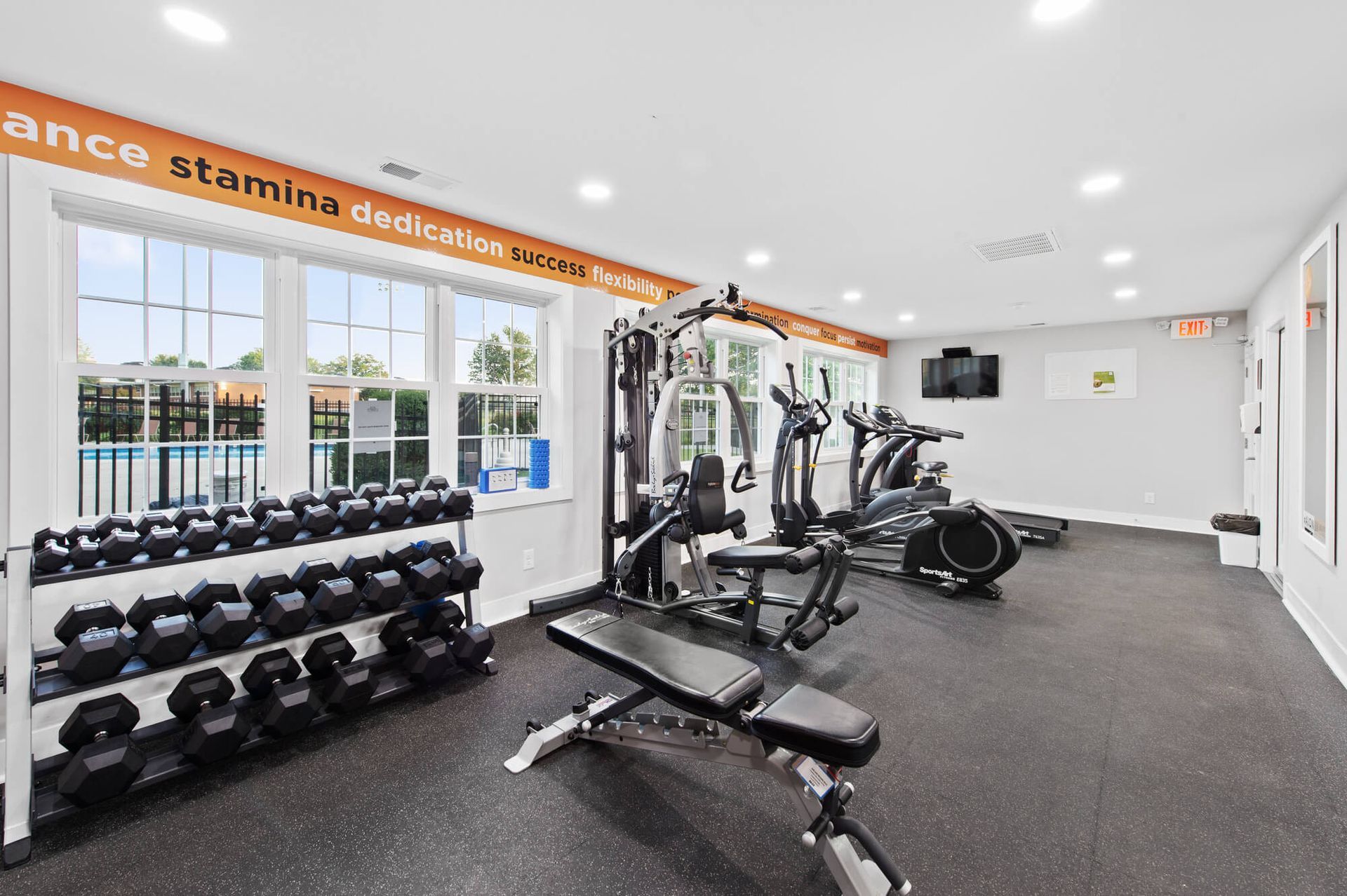 Indoor fitness center with dumbbells, a weight rack, benches and cardio machines.