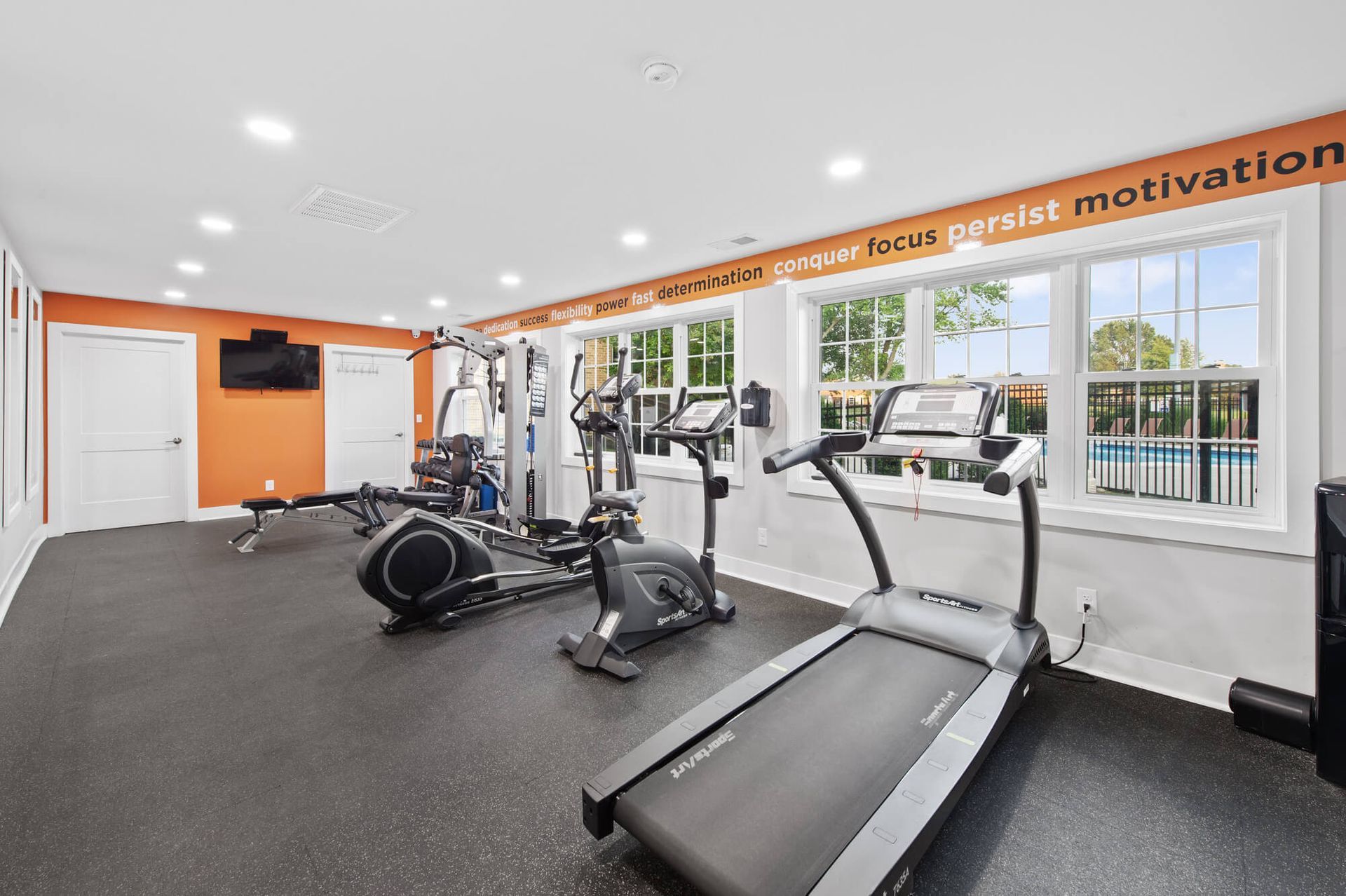 Bright apartment gym with cardio machines and orange accent wall.