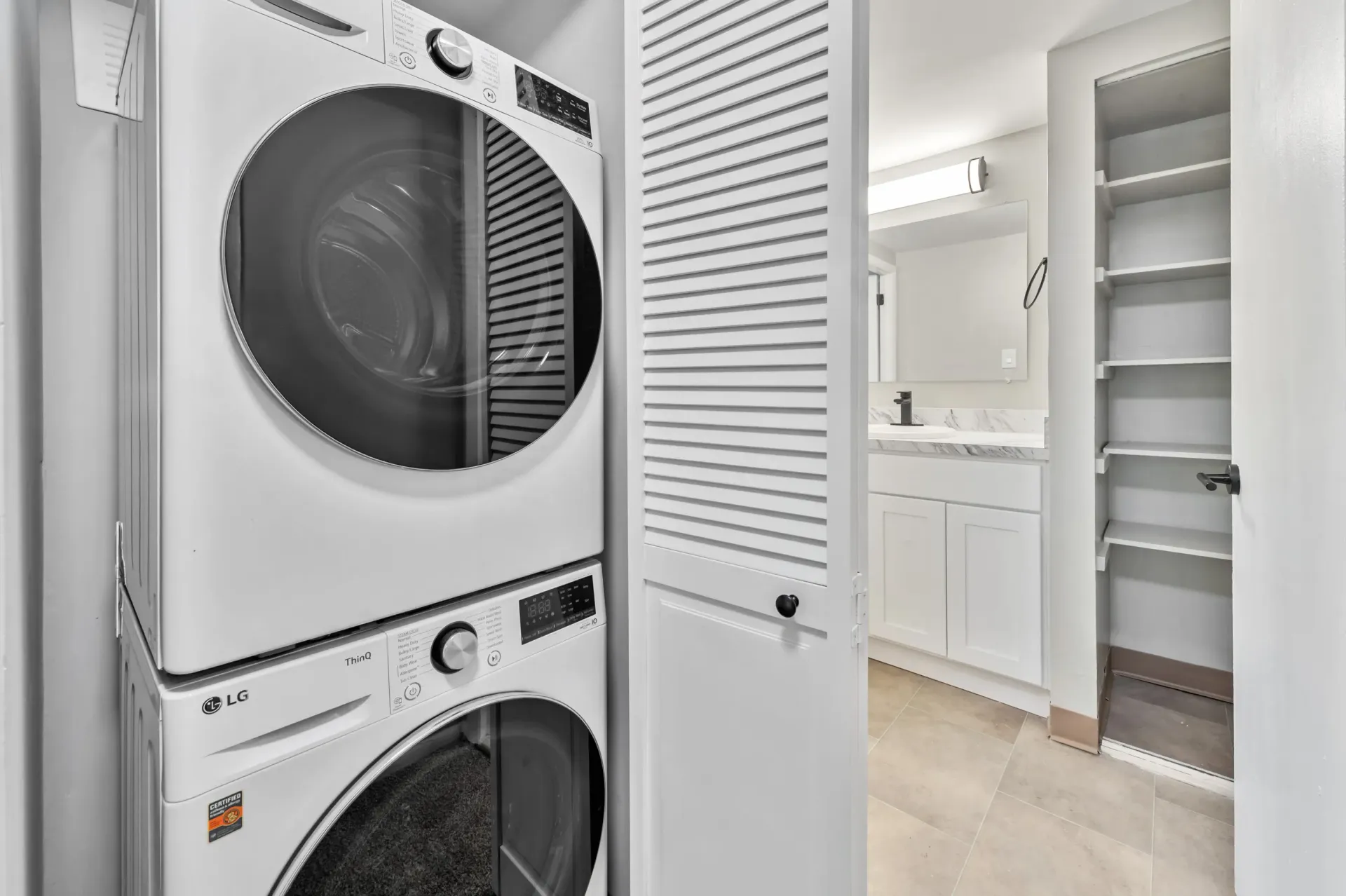 Stacked front-load washer and dryer in a laundry closet with a bathroom vanity nearby.