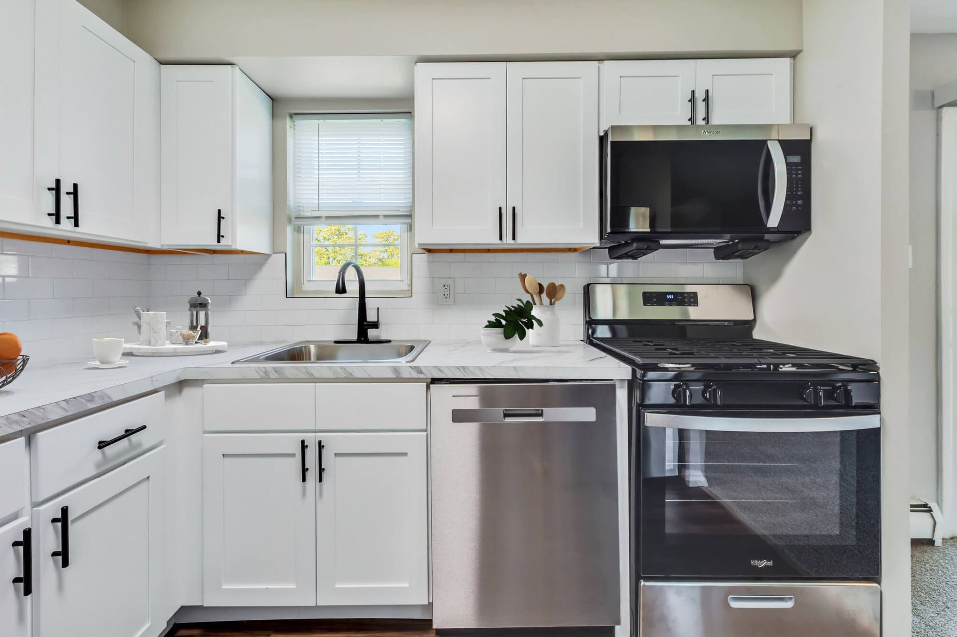 Modern kitchen with white cabinets, marble countertops, and stainless steel appliances.