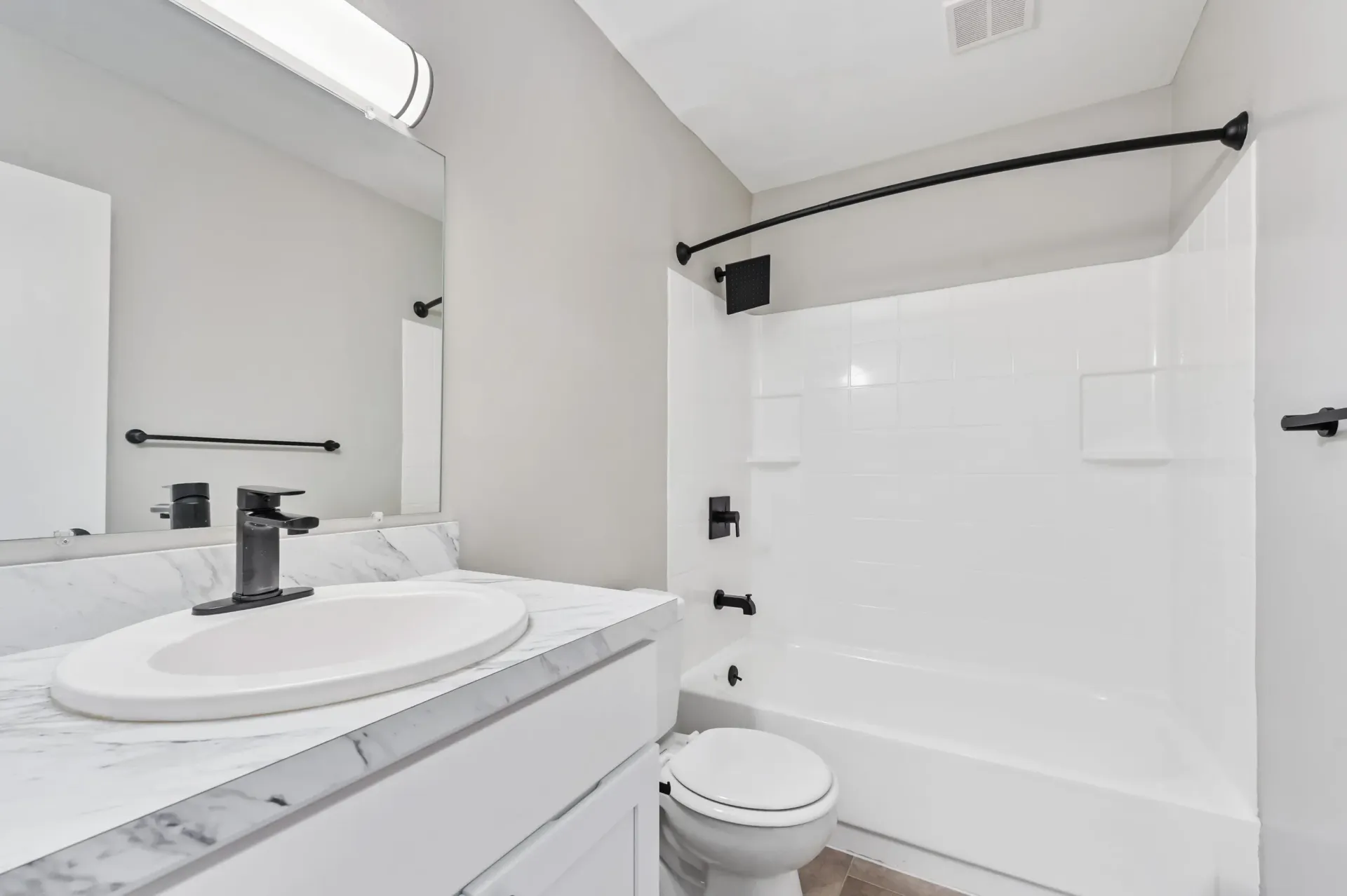 Bathroom with white sink, marble countertop, toilet, and tiled shower with black fixtures.