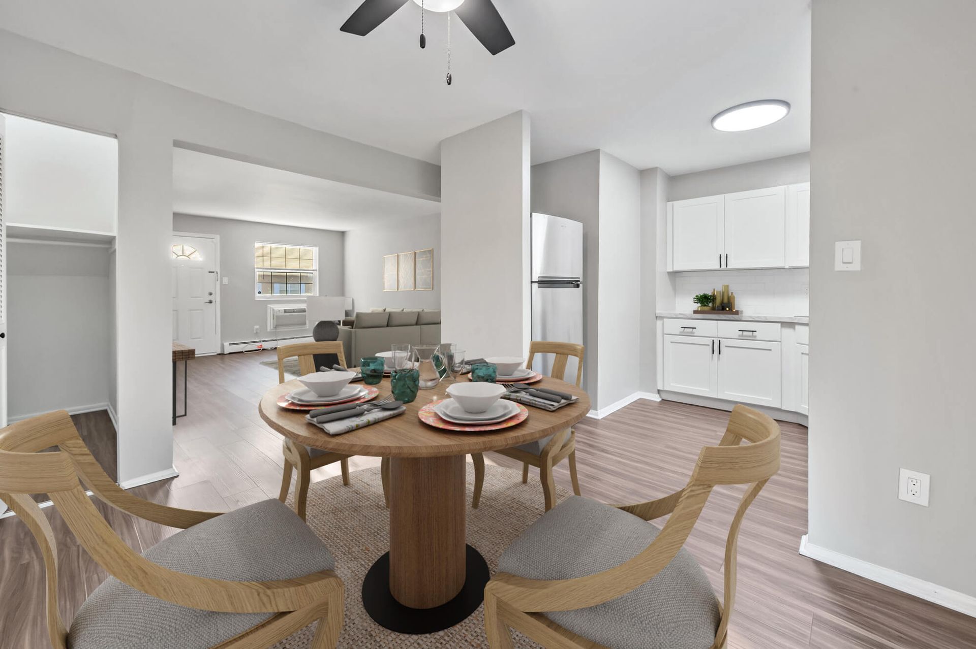 Open-concept apartment interior with round dining table, wooden chairs, and a white kitchen.