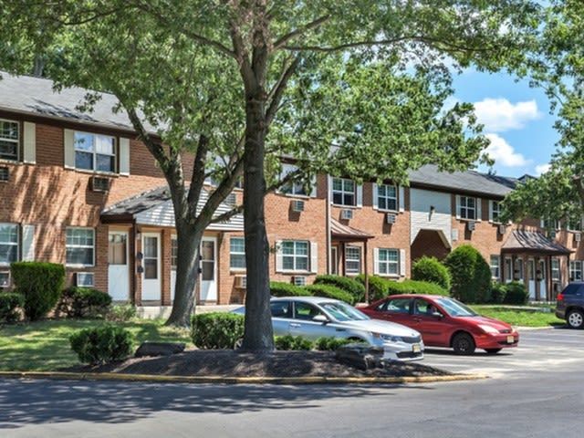 Exterior view of a brick apartment complex with trees and parked cars.