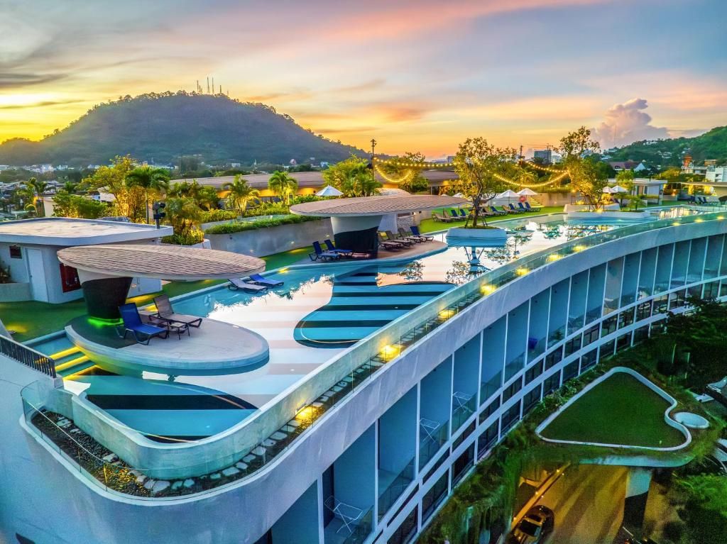 Rooftop pool at sunset overlooking green mountain, blue water, and white building with yellow lighting.