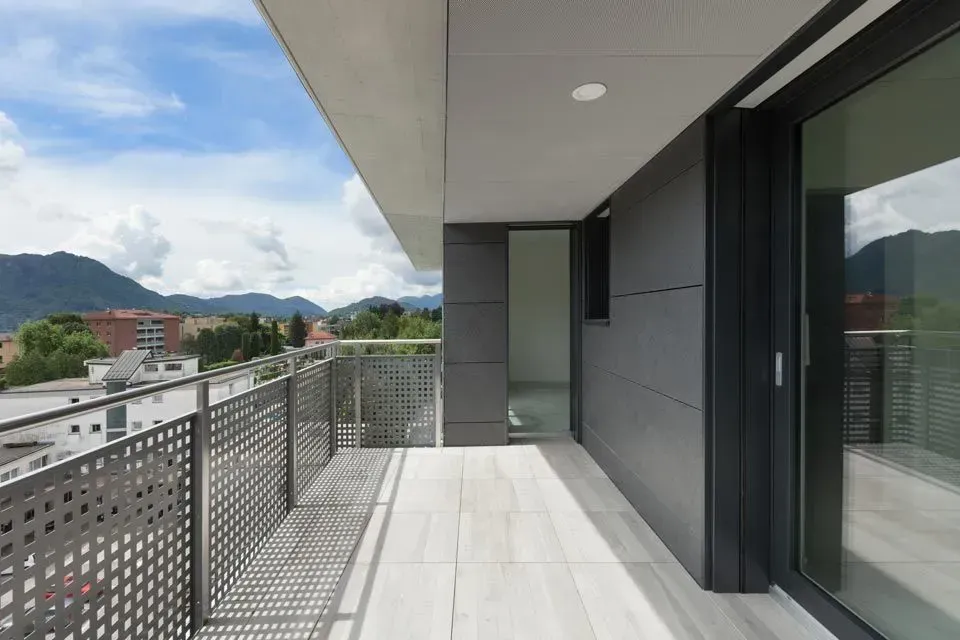 Ein moderner Balkon mit Metallgeländer, hellen Fliesenböden und dunkelgrauen Wänden mit Blick auf eine Berglandschaft.