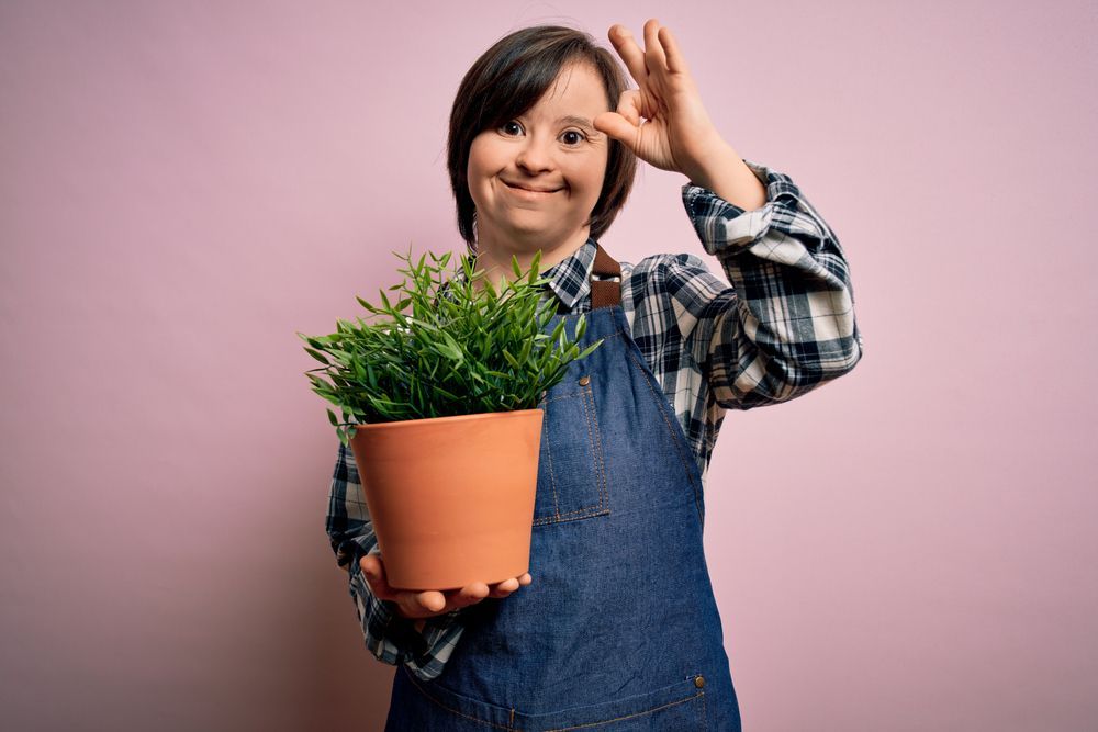 Woman With Down Syndrome in Denim Apron Holds Potted Plant — Sonke Support Pty. Ltd. in Mooloolaba, QLD