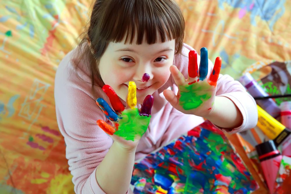 Girl With Down Syndrome Smiling, Showing Colorful Painted Hands — Sonke Support Pty. Ltd. in Mooloolaba, QLD