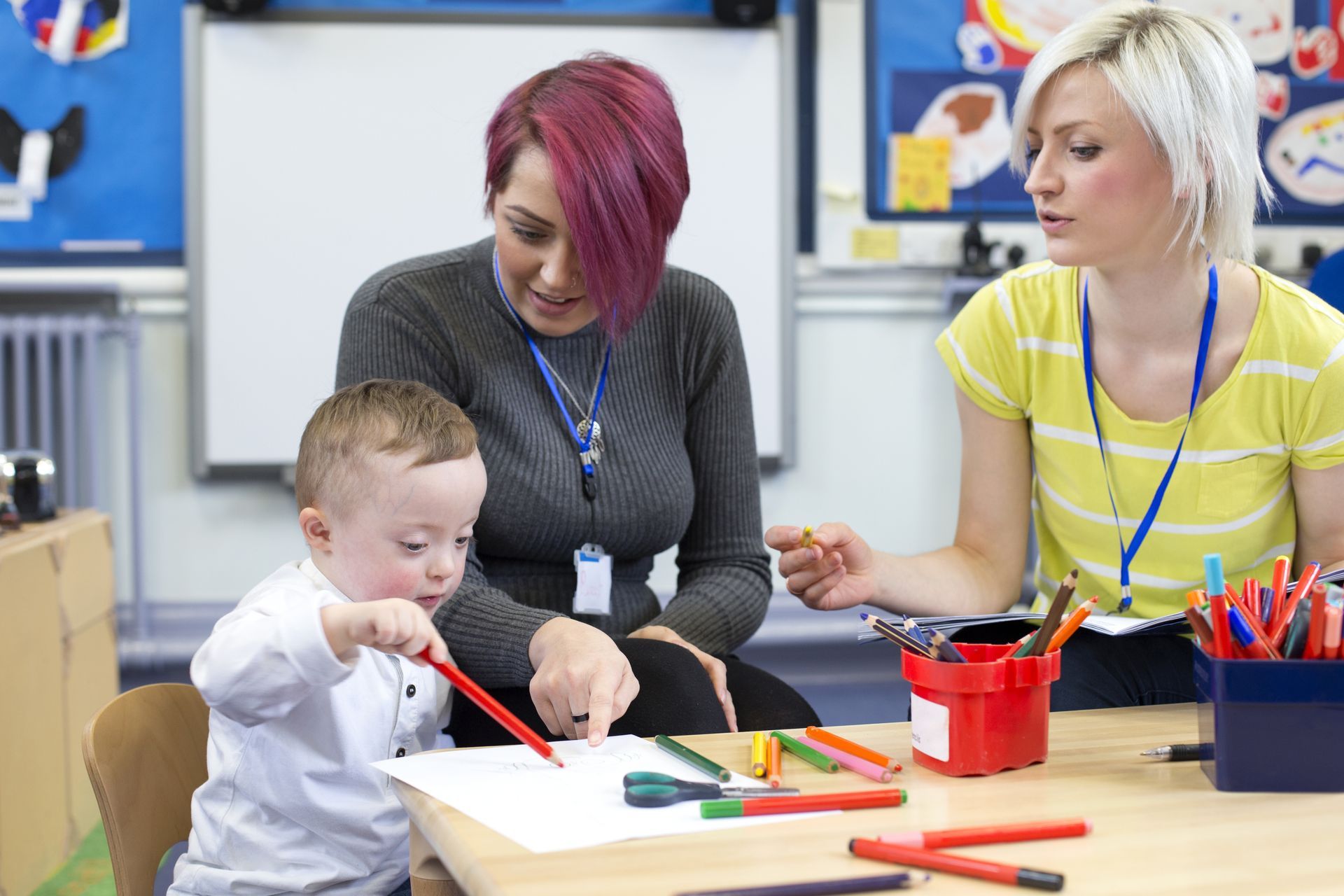 Child With Down Syndrome Draws at a Table With Two Teachers — Sonke Support Pty. Ltd. in Noosa Heads, QLD