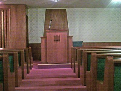 A church interior with a wooden pulpit, rows of pews, and a microphone stand.