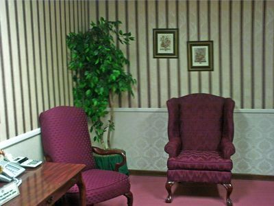 Two burgundy chairs in a room with striped wallpaper, two framed pictures, and a potted plant.