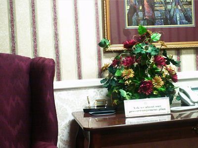 Desk with flowers and sign. Burgundy chair and striped wallpaper in background.