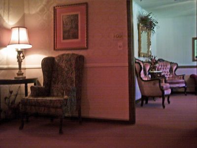 A waiting room with patterned chair, lamp, framed art, and partial view of more seating.