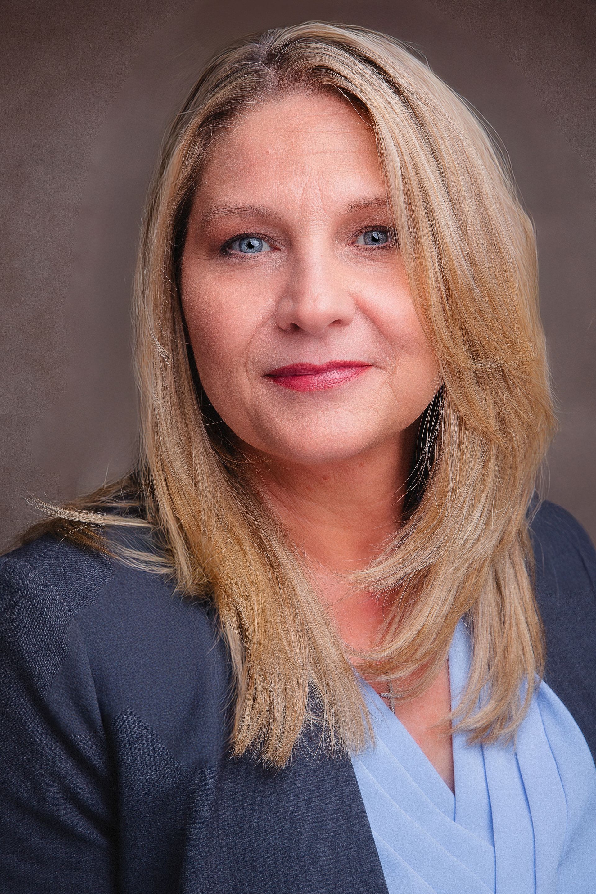 A woman with long blonde hair is wearing a blue shirt and a gray jacket.
